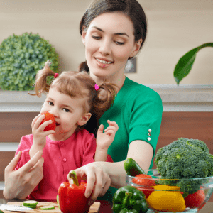 little girl sits in mom's lap and snacks on eye healthy vegetables