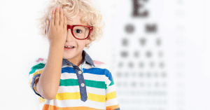 kid covers eye in front of eye chart for eye doctor exam