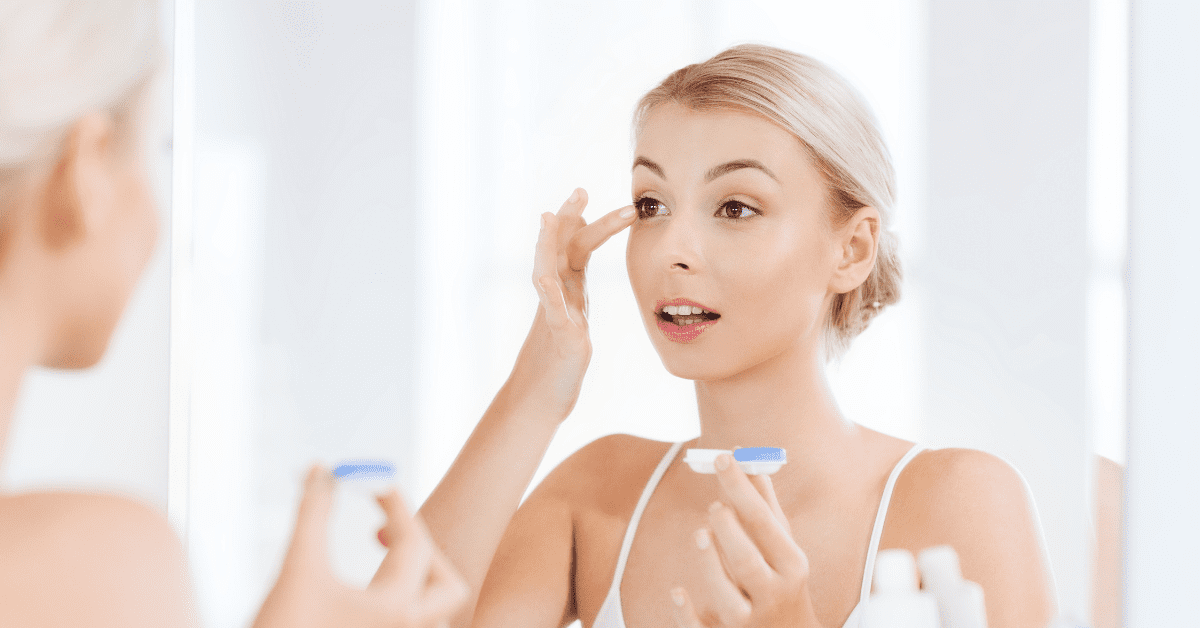 woman looks into mirror as she places contact lens into eye