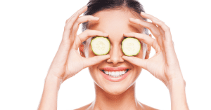 woman holds cucumber in front of eyes while smiling to demonstrate healthy eye habits