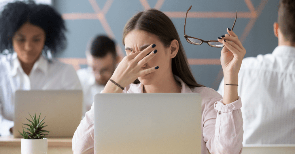 woman working on computer takes glasses off to rub dry eyes