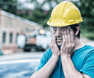 construction worker with safety glasses and hard hat rubbing eyes